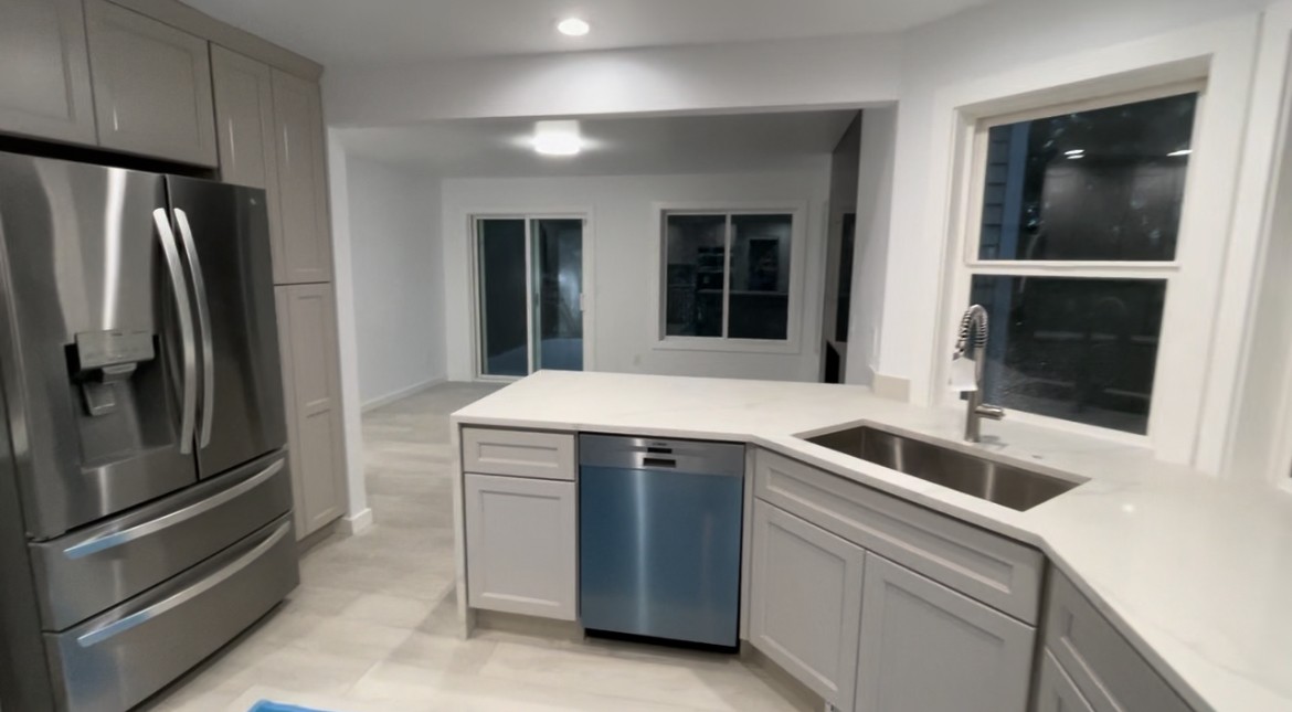 Open kitchen with grey shaker cabinets, quartz peninsula and stainless appliances