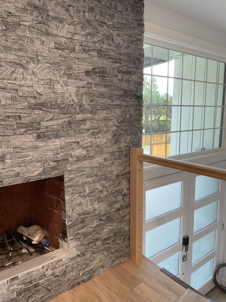 Floor-to-ceiling grey stacked-stone fireplace surround next to a large window