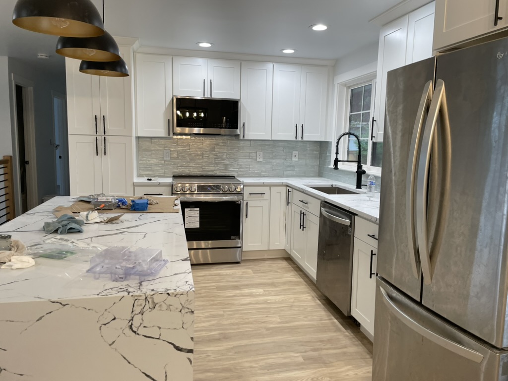 Kitchen with white shaker cabinets, glass tile backsplash, marble waterfall island and stainless appliances